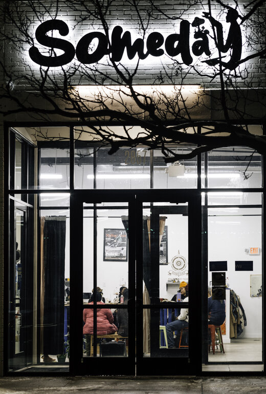 Nighttime view of the gallery, with the Someday sign backlit and partially hidden by craggy tree branches.